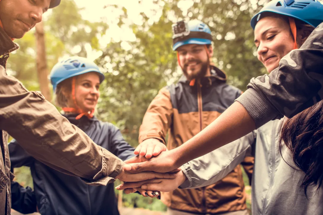 A group of ropes course staff in helmets stacking their hands together in a team huddle