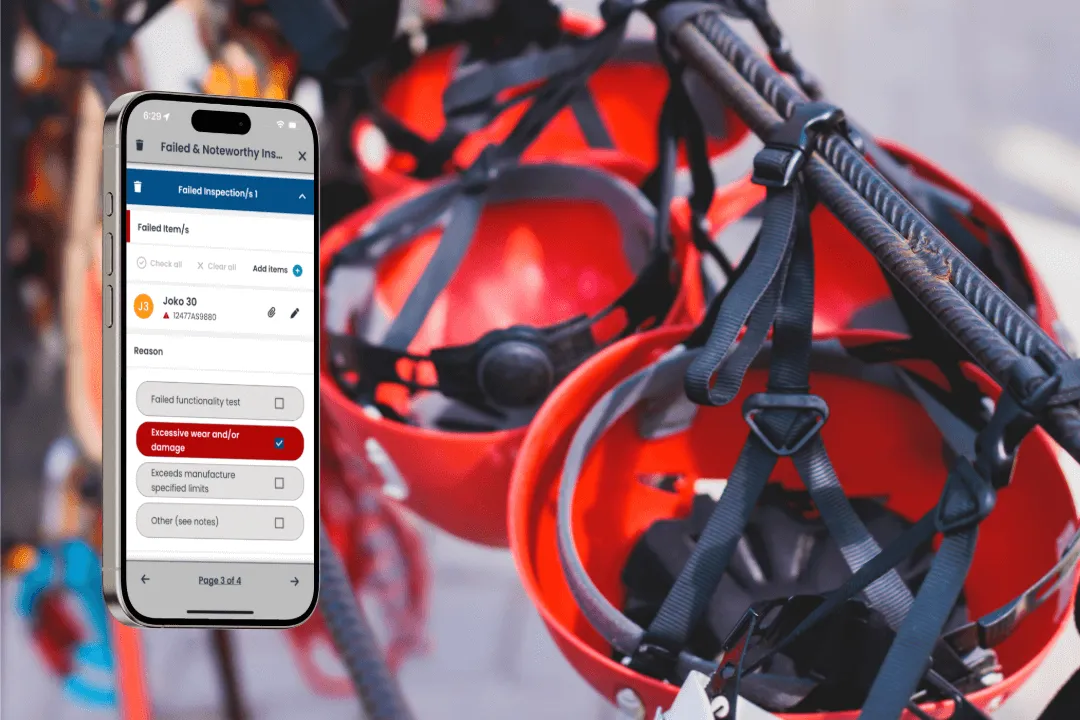 A phone showing a failed PPE inspection screen next to red climbing helmets and harnesses